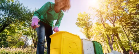 Photographie d'une personne vidant un bac jaune de recyclage dans un parc ensoleillé